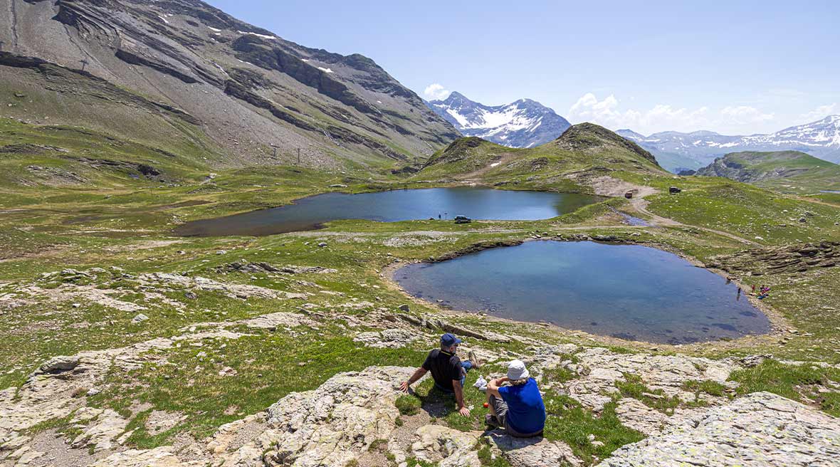 Two hikers enjoying a rest by lakes up in the snow-capped mountains